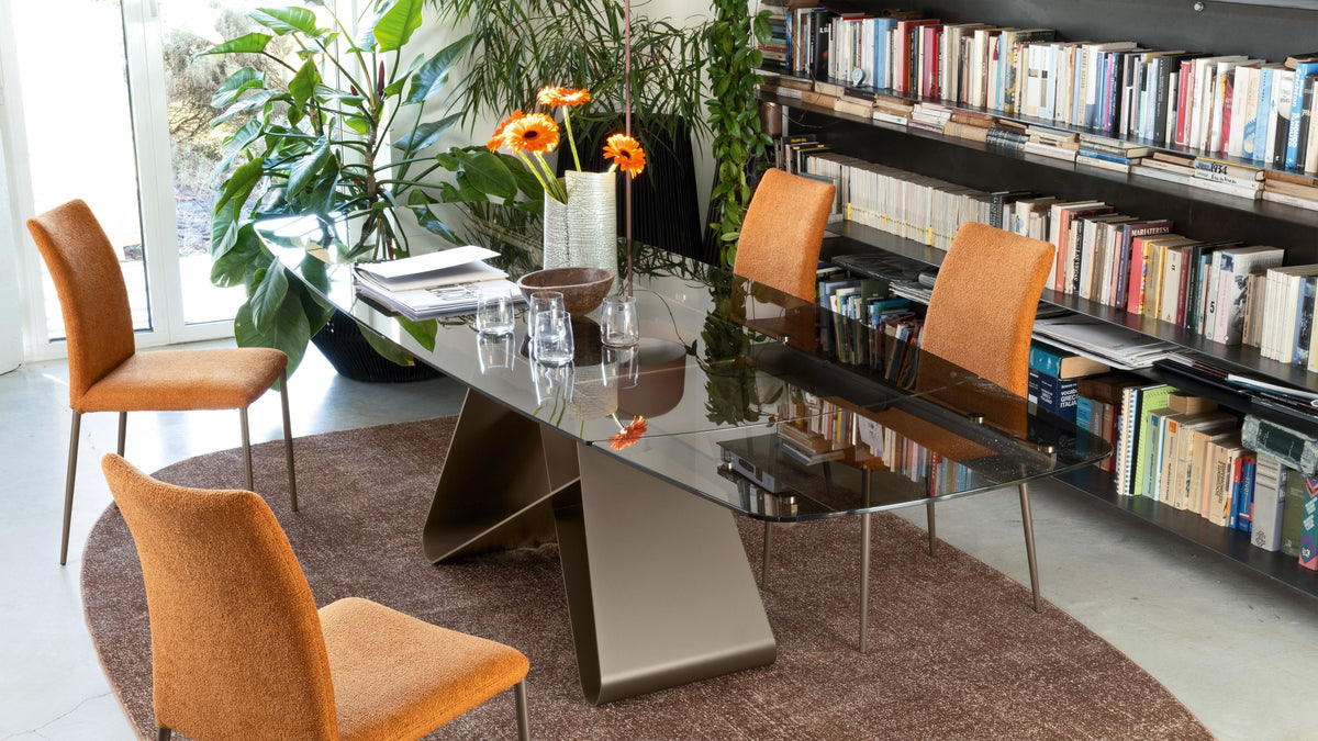 Connubia Gemini extendable dining table with orange Atlas dining chairs on a Vully rug beside a library wall