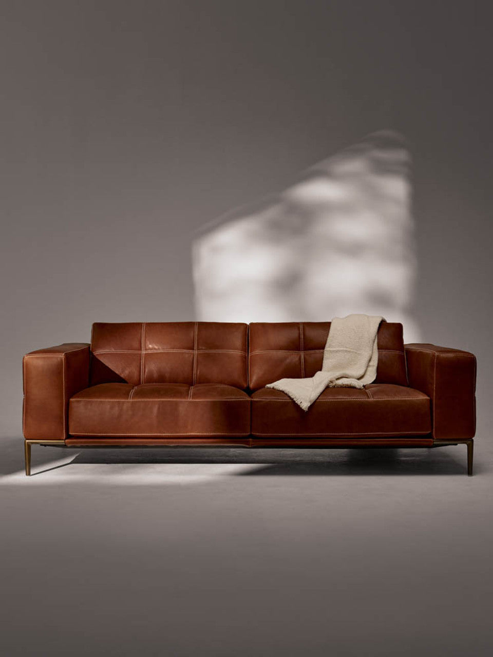 American Leather Barcelona sofa in cognac leather with a cream throw, against a softly lit grey wall