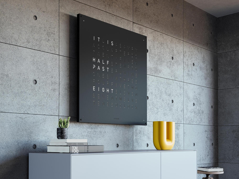 QLOCKTWO EARTH 90 word clock in black reading IT IS HALF PAST EIGHT on a concrete wall