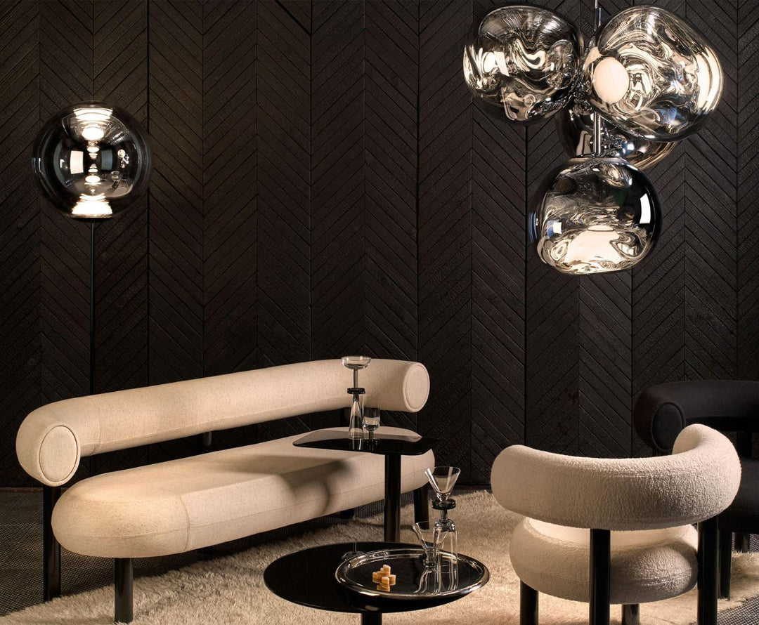 Tom Dixon Melt chandelier glowing above a cream curved sofa in a dark lounge