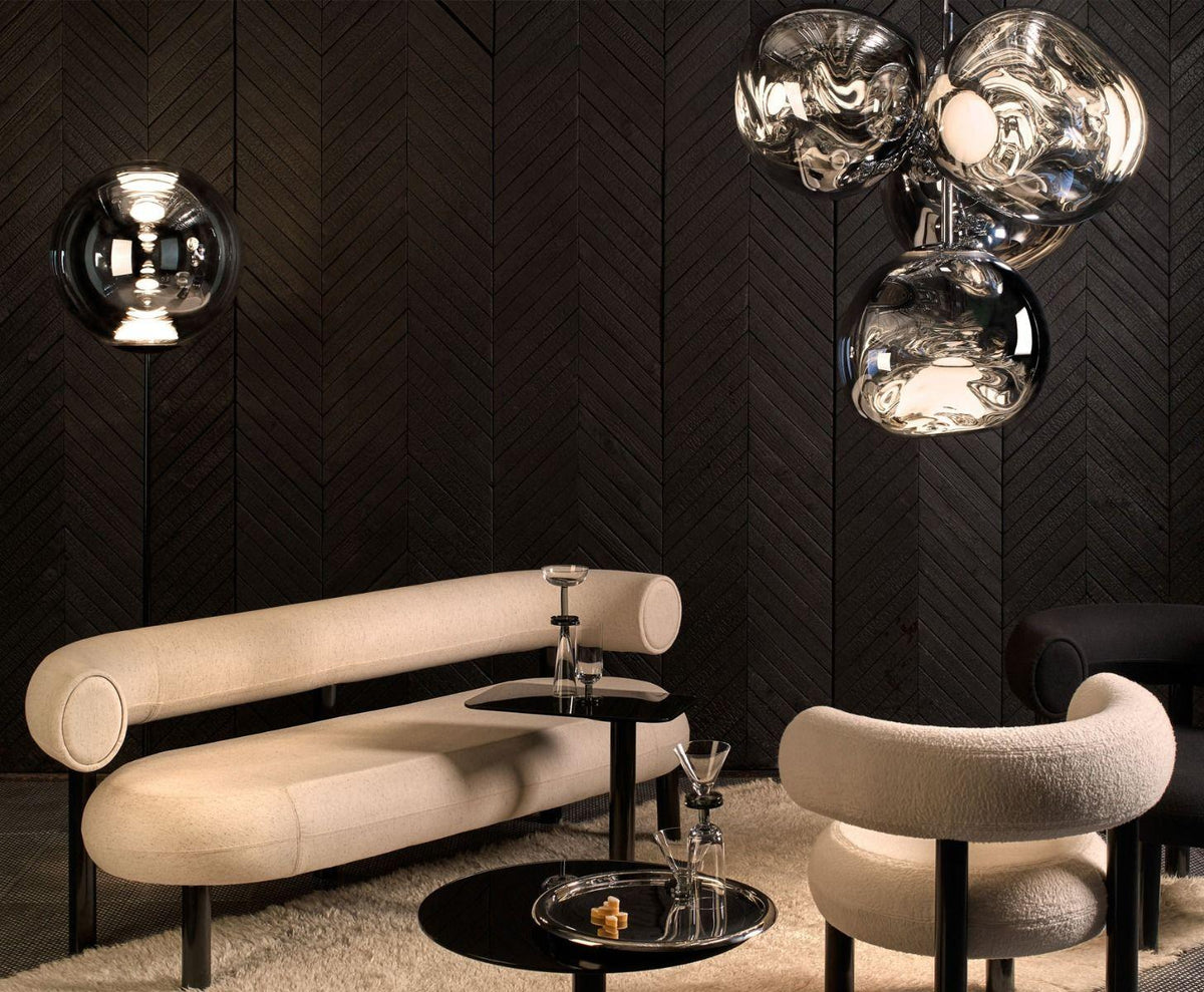 Tom Dixon Melt chandelier glowing above a cream curved sofa in a dark lounge