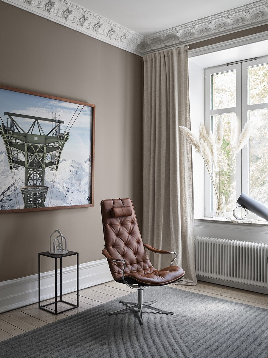 Conform Bravo high-back chair in brown leather on a polished swivel base, shown by a tall window in a furnished living room