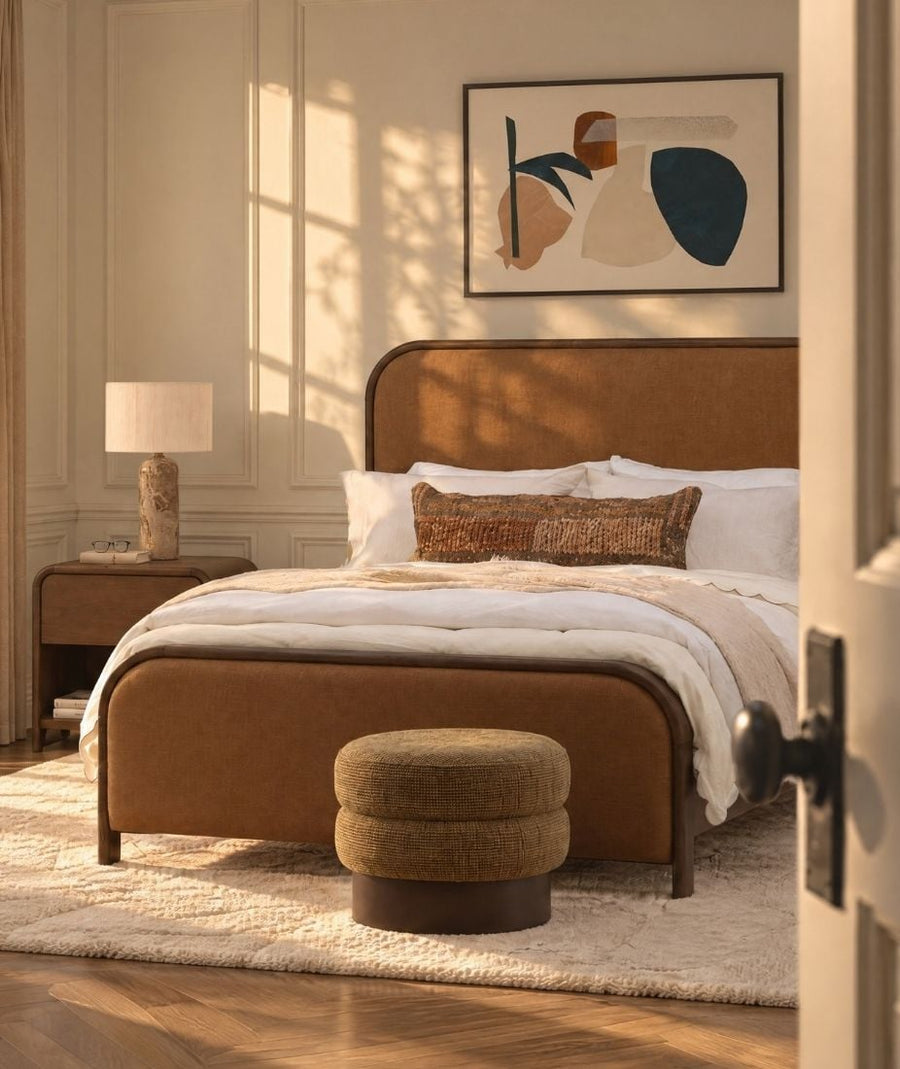 Warm tan upholstered bed and wood nightstand in a sunlit cream bedroom