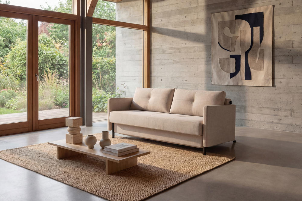 Cubed sofa bed with arms in beige fabric in a sunlit room with floor-to-ceiling windows