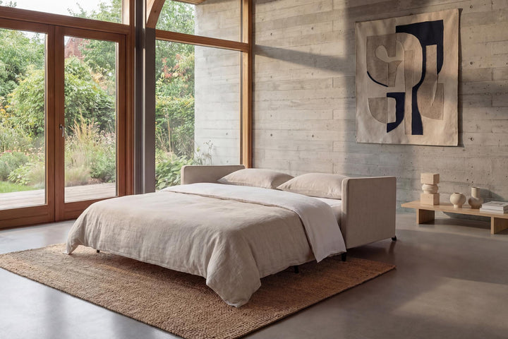 Cubed sofa bed with arms opened into a bed in a sunlit room with large windows