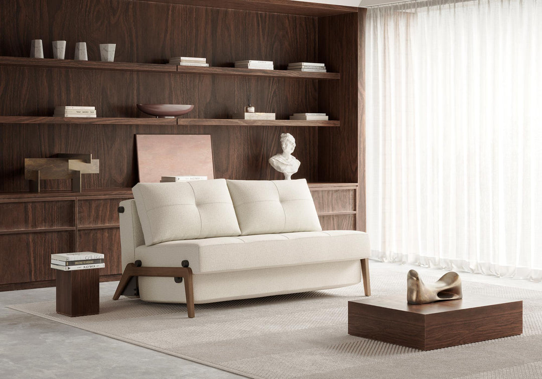Cream Cubed sleeper sofa with dark wood legs in front of a dark wood shelving wall