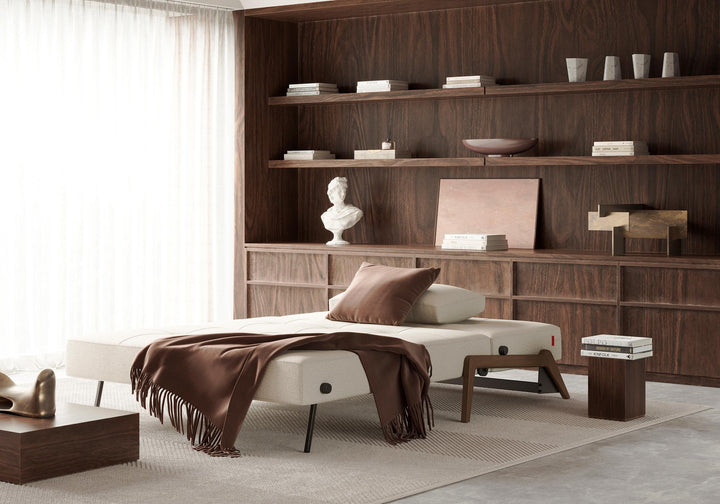 Cubed sleeper sofa with dark wood legs opened into a bed with a brown throw