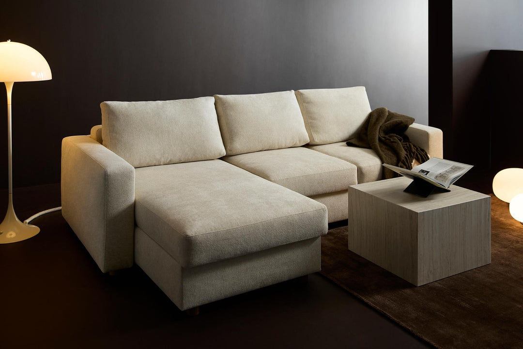Cream Neah sleeper chaise sectional with pillows in a dark room with floor lamp