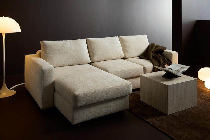 Cream Neah sleeper chaise sectional with pillows in a dark room with floor lamp