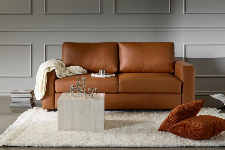 Cognac leather Neah queen sleeper sofa on a white shag rug with pillows