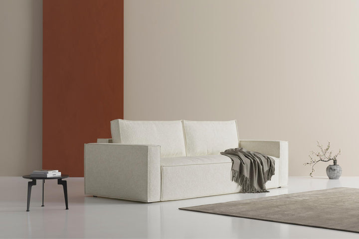 Cream Newilla sleeper sofa with a throw against a rust accent wall