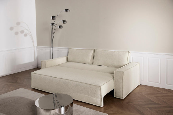Cream Newilla sleeper sofa opened into a bed beside an arc floor lamp