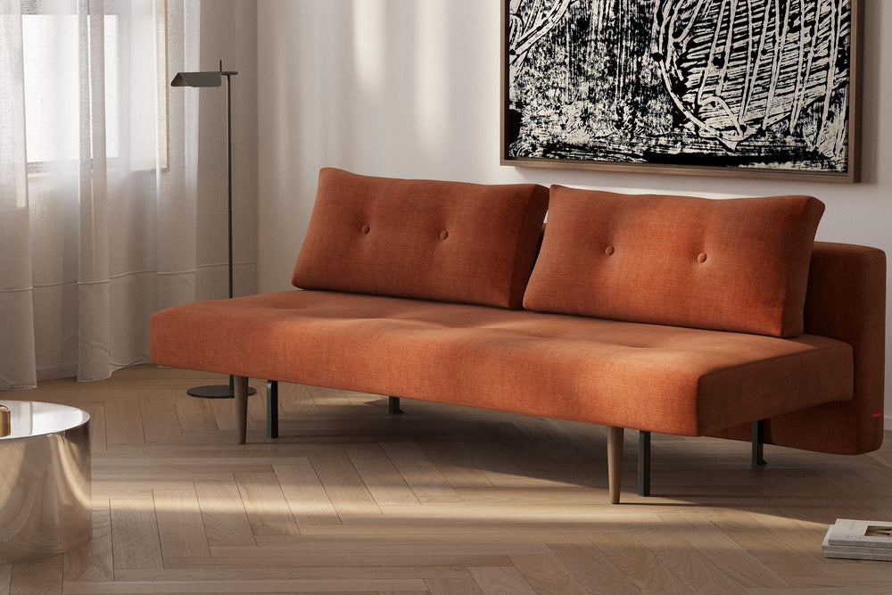 Rust Recast sleeper sofa with button-tufted cushions and dark wood legs below abstract art