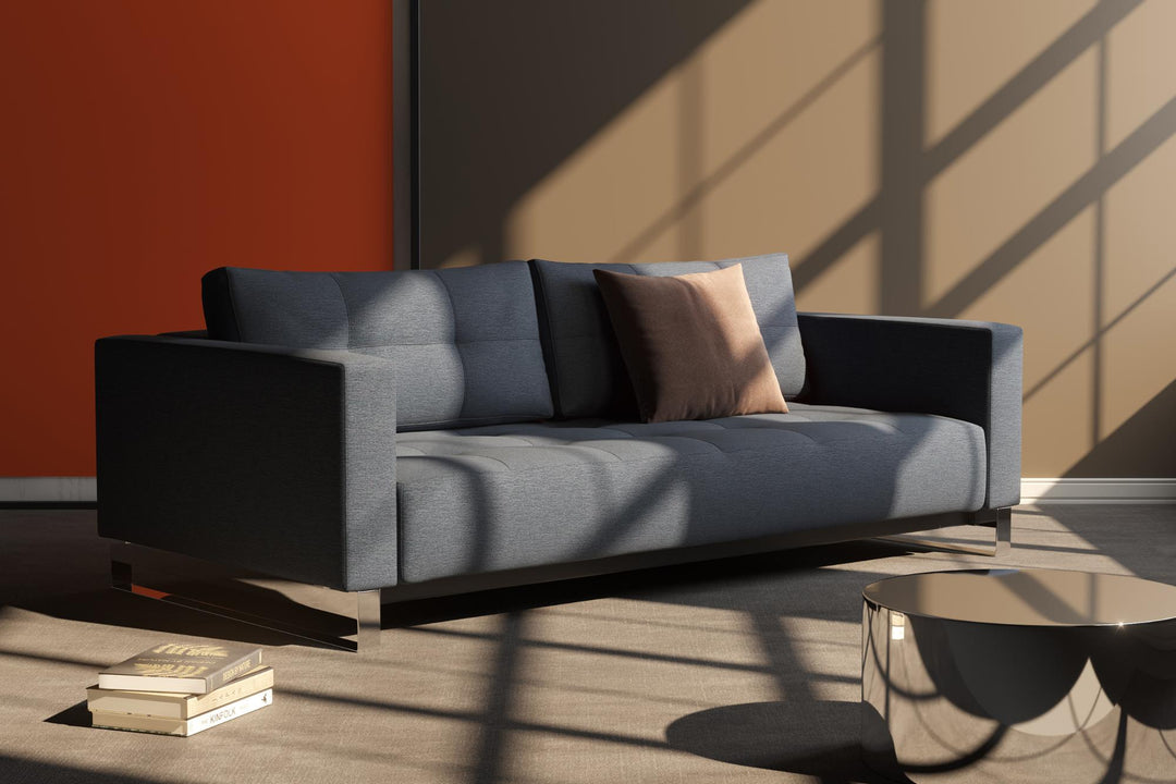 Charcoal Cassius D.E.L. sleeper sofa with chrome legs in sunlight against an orange wall