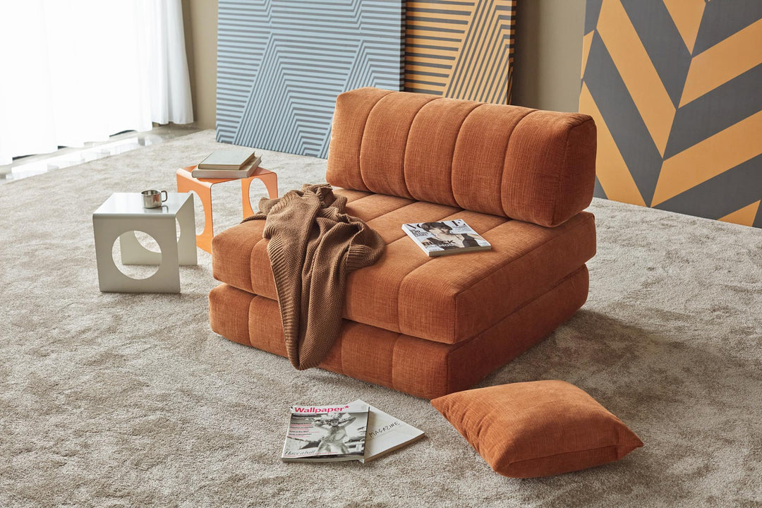Orange CozyPad chair with scattered magazines and pillows by a patterned wall