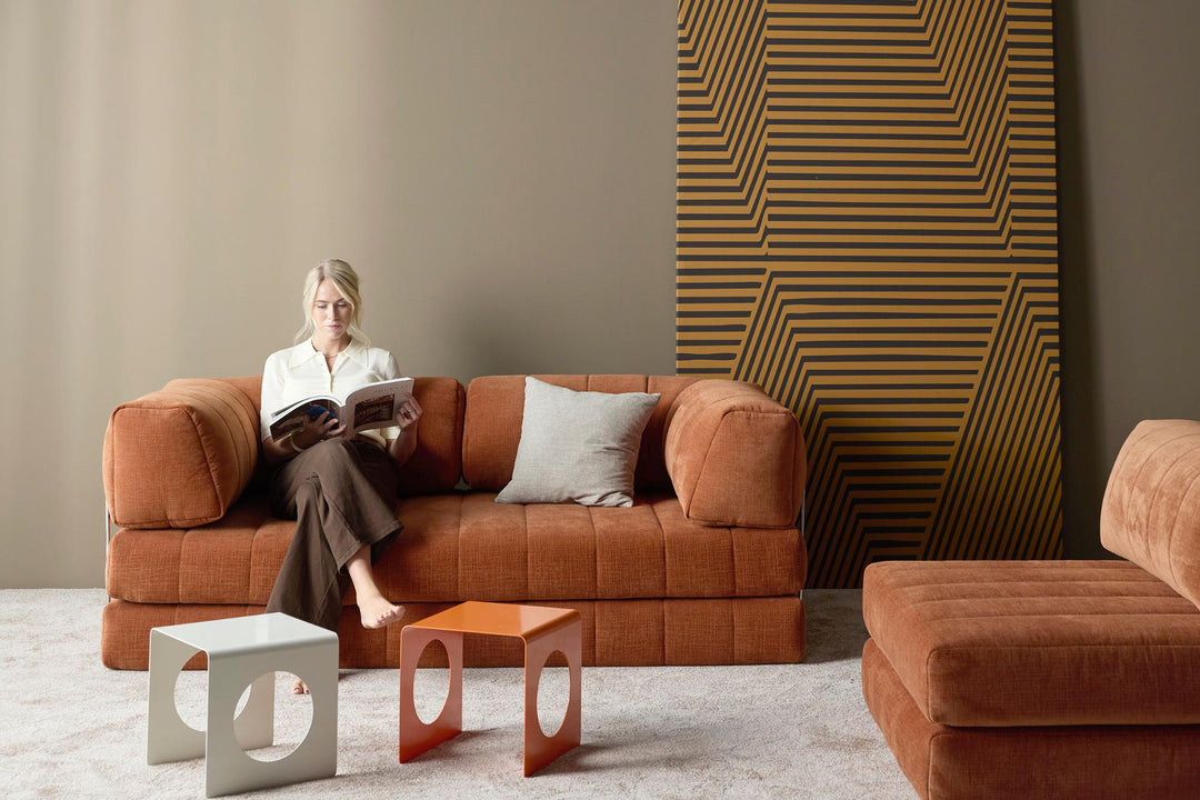 Woman reading on an orange CozyPad sleeper sofa with arms in a room with patterned wall panels