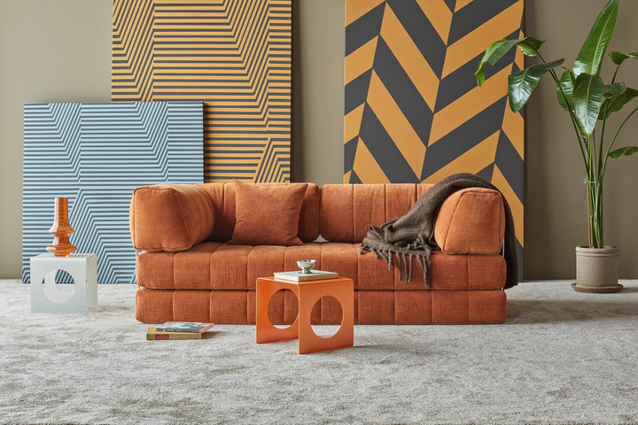 Orange CozyPad sleeper sofa with arms beside a plant and patterned wall panels