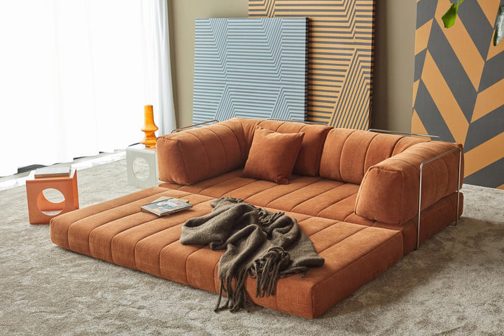 Orange CozyPad sleeper sofa with arms laid flat as a lounge bed with a throw