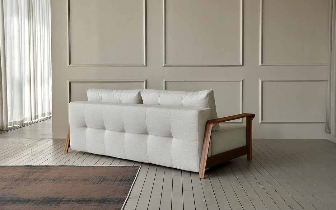 Ran D.E.L sofa bed with tufted seat and wood arms against a paneled wall
