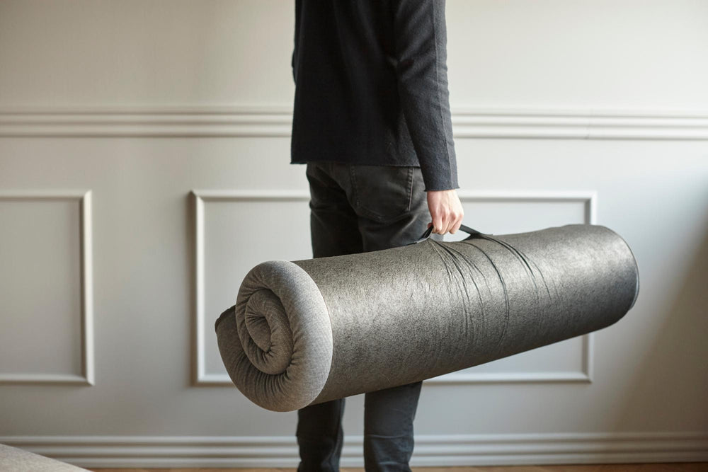 Person carrying a rolled Innovation Living pillow topper in its storage bag