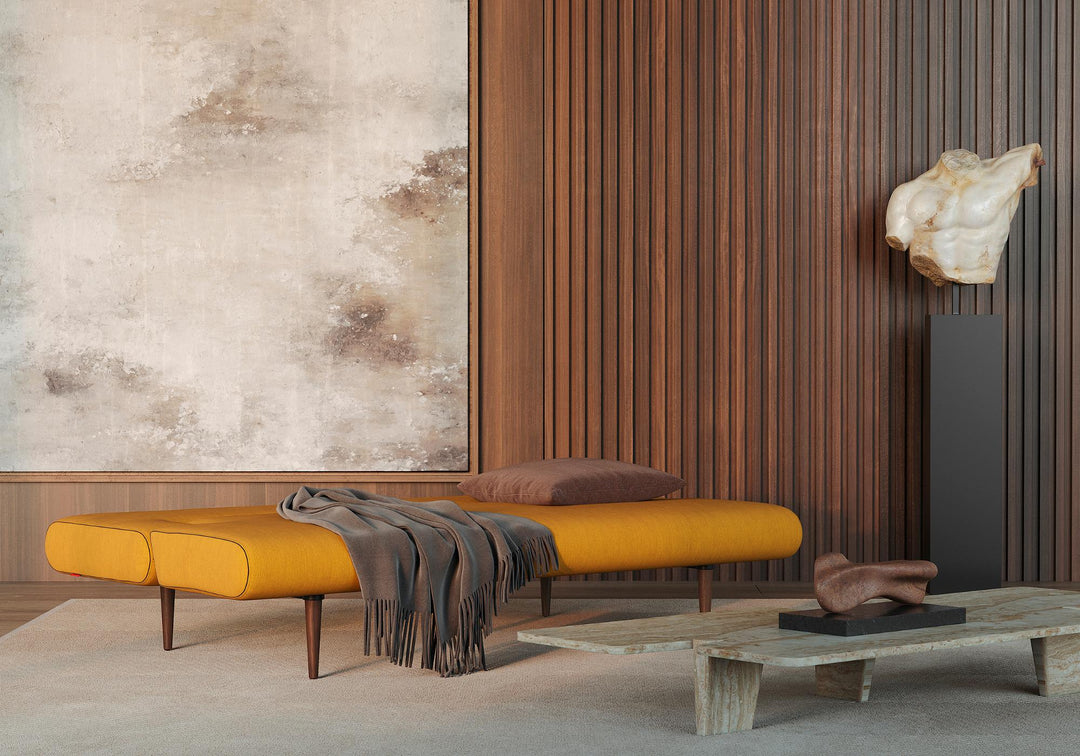 Mustard Unfurl sleeper sofa reclined with a throw in a room with wood slat wall