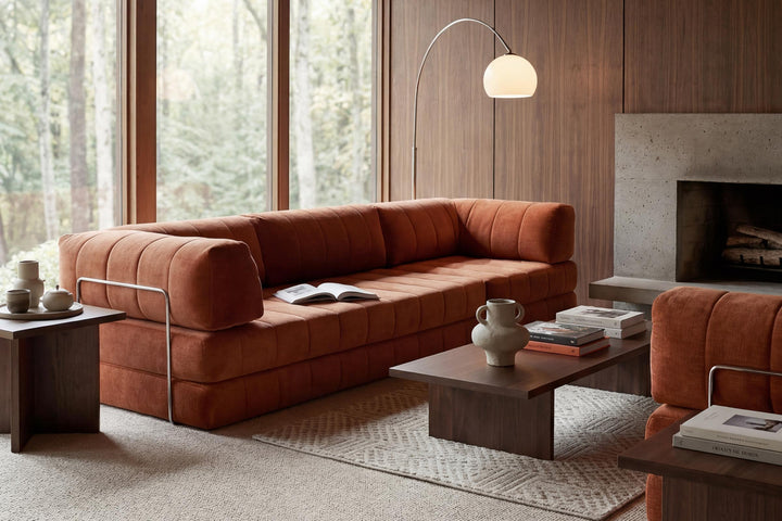 CozyPad Sleeper Sofa Grand with arms by Innovation Living in rust orange velvet with a dark wood coffee table by a fireplace and tall windows