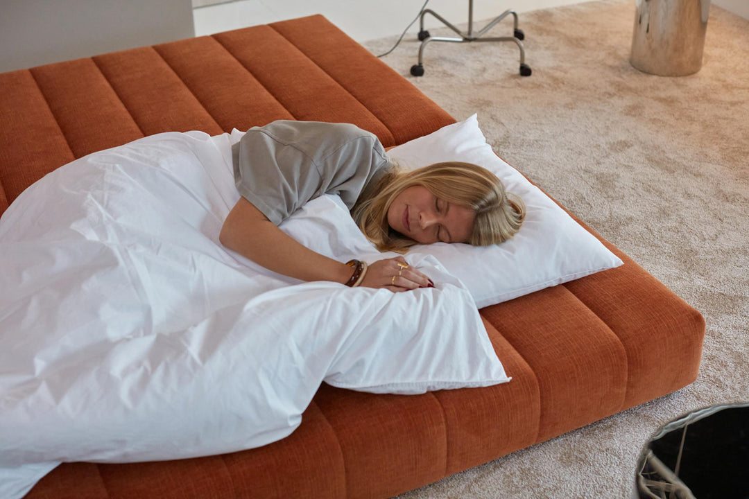 CozyPad Sleeper Sofa Corner with arms by Innovation Living in rust orange velvet with a woman sleeping under a white duvet