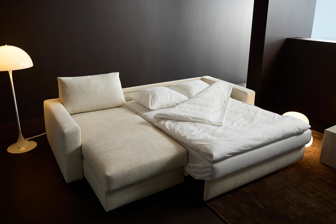 Neah Sleeper Chaise Sectional by Innovation Living opened into a bed with white bedding beside a globe floor lamp