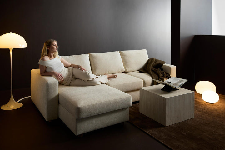 Neah Sleeper Chaise Sectional by Innovation Living in cream with a woman relaxing on the chaise in a dark room