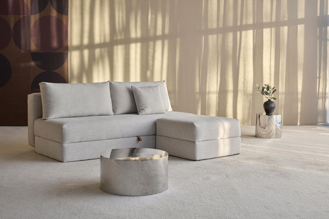 Osvald Sleeper Sofa by Innovation Living in light grey with chaise and a round metal side table in sunlit room