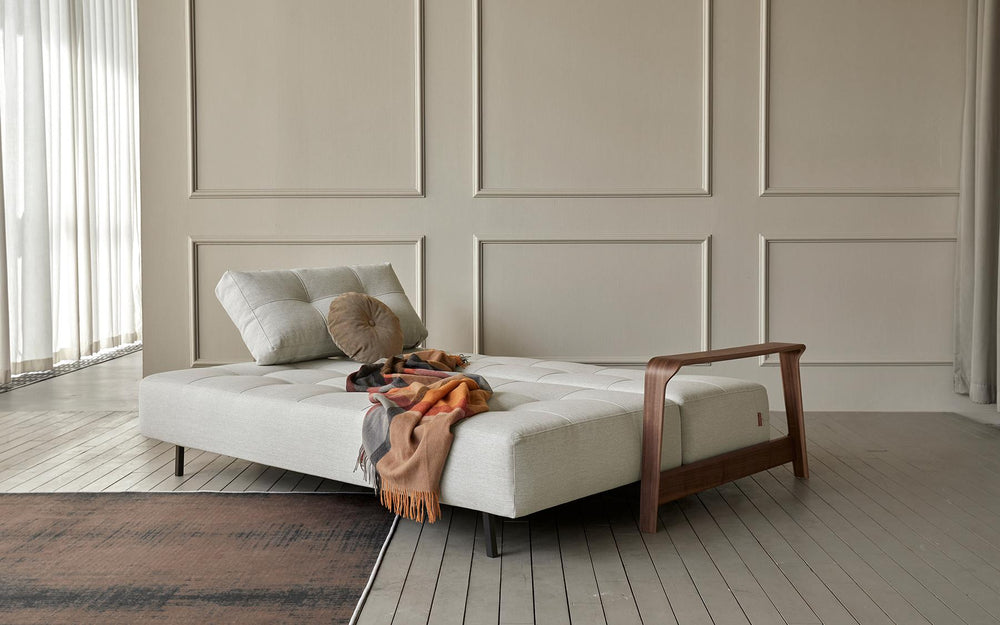Ran D.E.L Sofa Bed by Innovation Living opened as a bed with a rust throw in a white panelled room on a grey rug