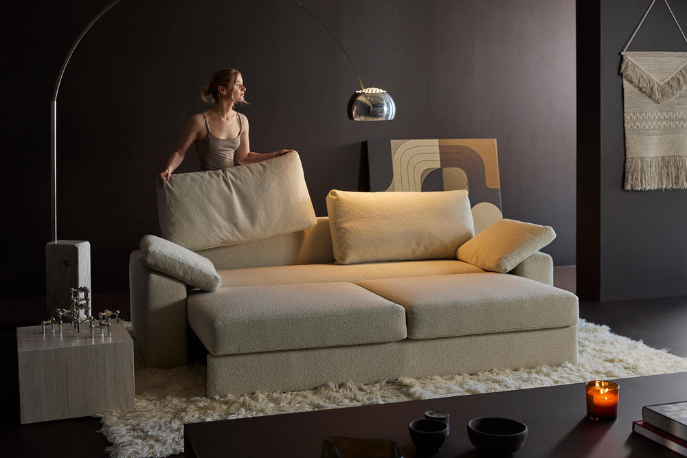 Vilander Sleeper Sofa by Innovation Living in beige with a woman adjusting the cushions under an arc lamp