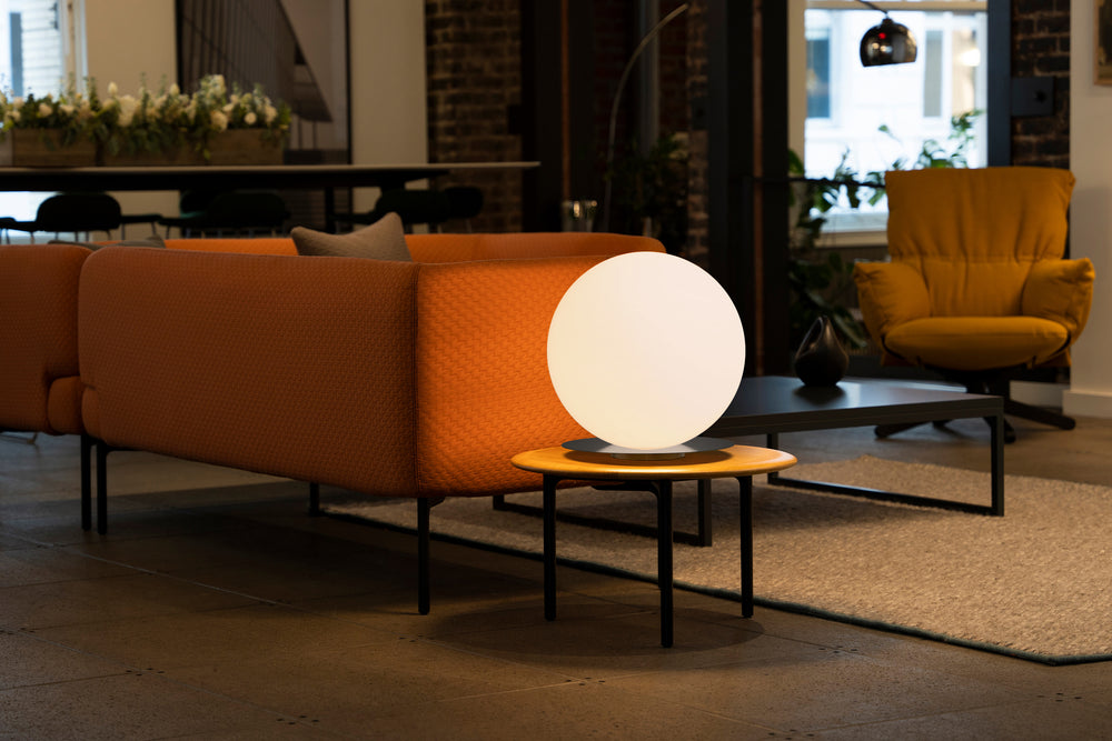 Bola Sphere Table Lamp by Pablo Designs in a living room beside an orange sofa